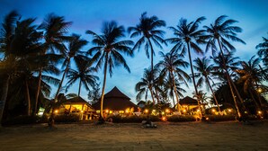 Un resort en la playa al anochecer, con palmeras y edificios iluminados.