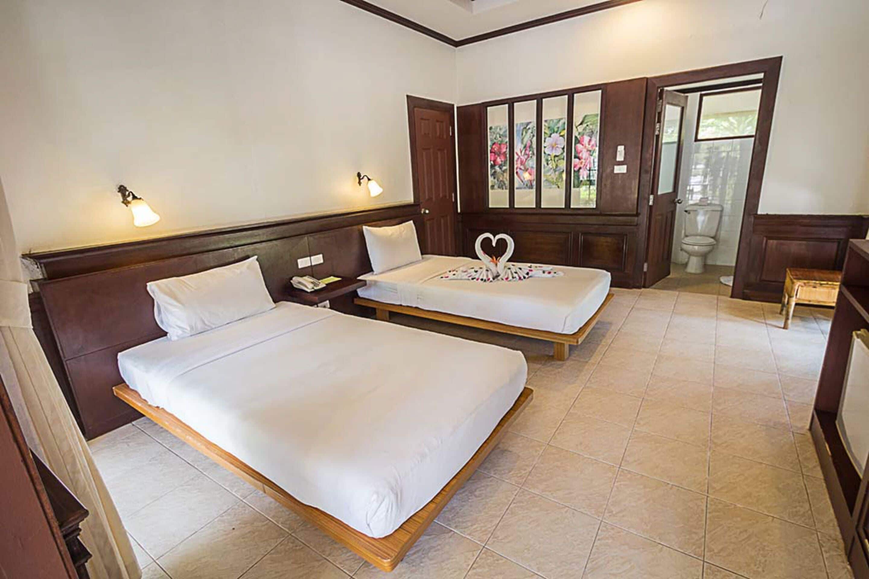 Habitación de hotel con dos camas individuales, cabecero de madera, mesita de noche y ventana con cortinas florales, con vista al baño.