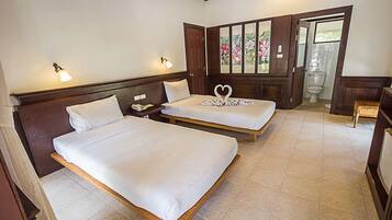 Habitación de hotel con dos camas individuales, cabecero de madera, mesita de noche y ventana con cortinas florales, con vista al baño.