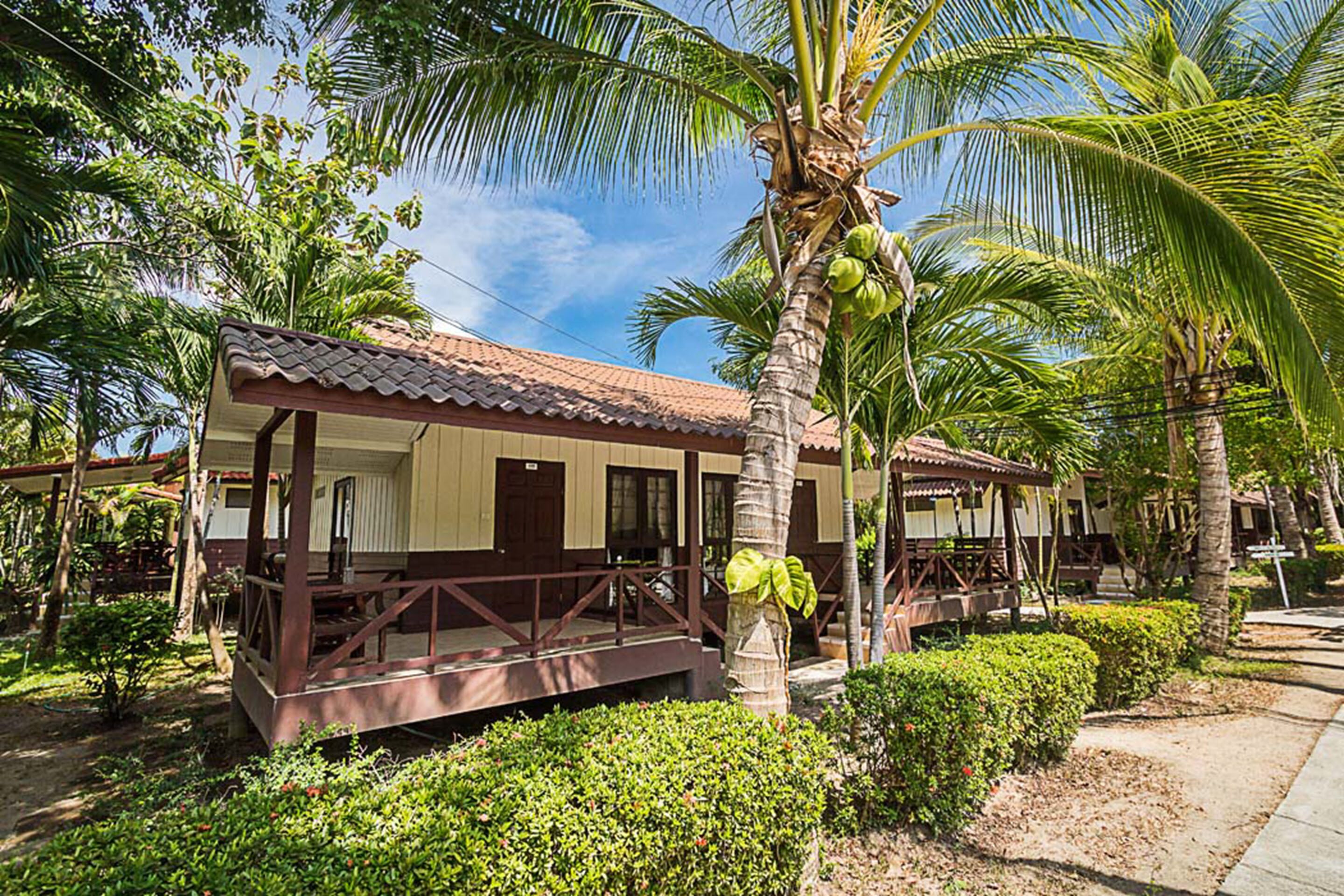 A bungalow-style building with a tiled roof, surrounded by lush greenery and palm trees.