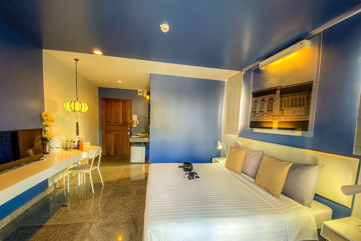 A modern hotel room with a large bed, a desk, and a kitchenette.
