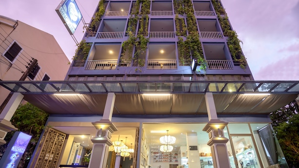 A multi-story building with a modern design, featuring balconies with greenery, a glass entrance, and a sign indicating it is a hotel. - Sino Inn (Phuket)