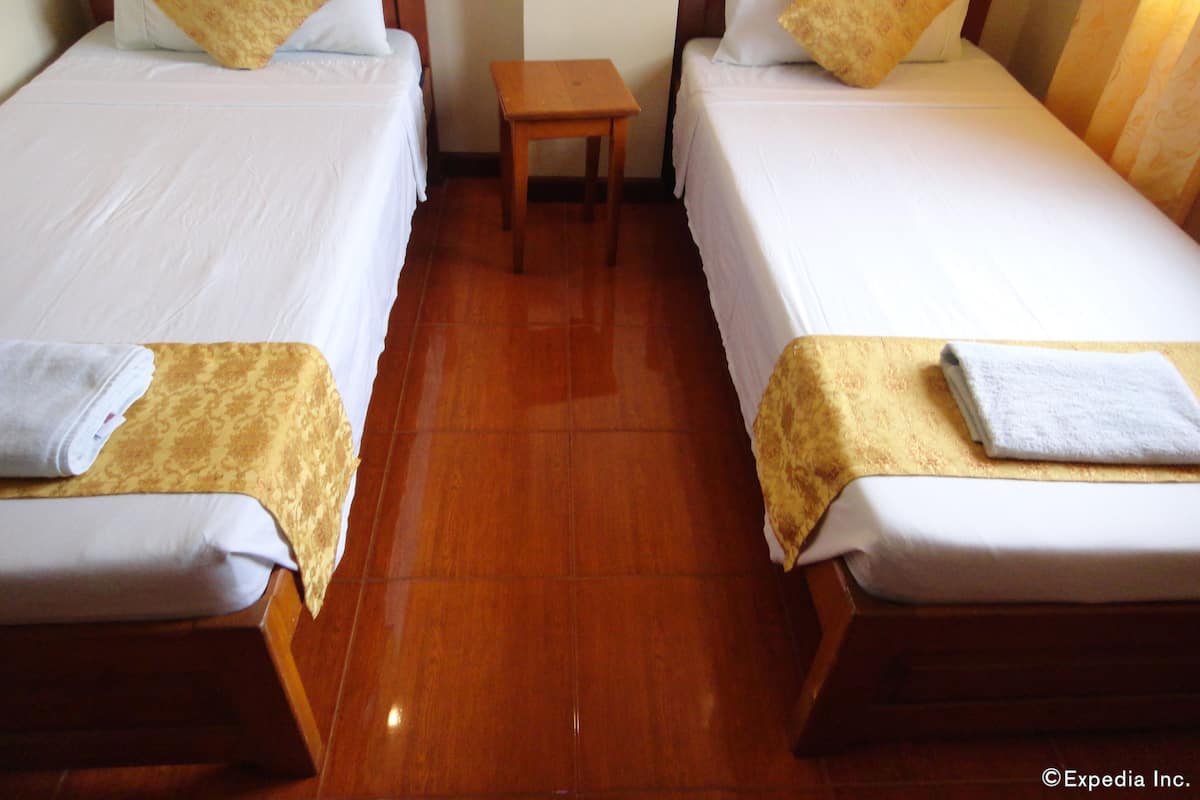 A hotel room with two single beds, a small wooden nightstand, and a tiled floor.