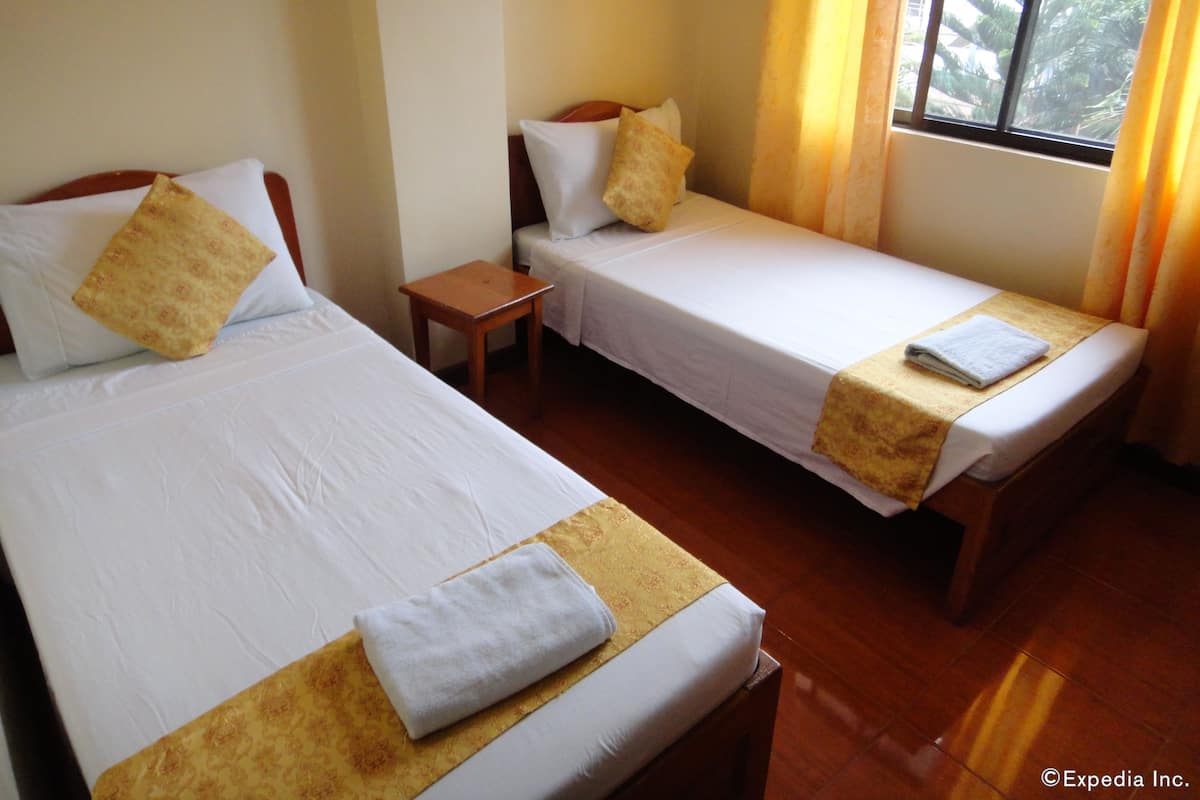 Two single beds with white linens and yellow decorative borders, a wooden nightstand, and a window with curtains.