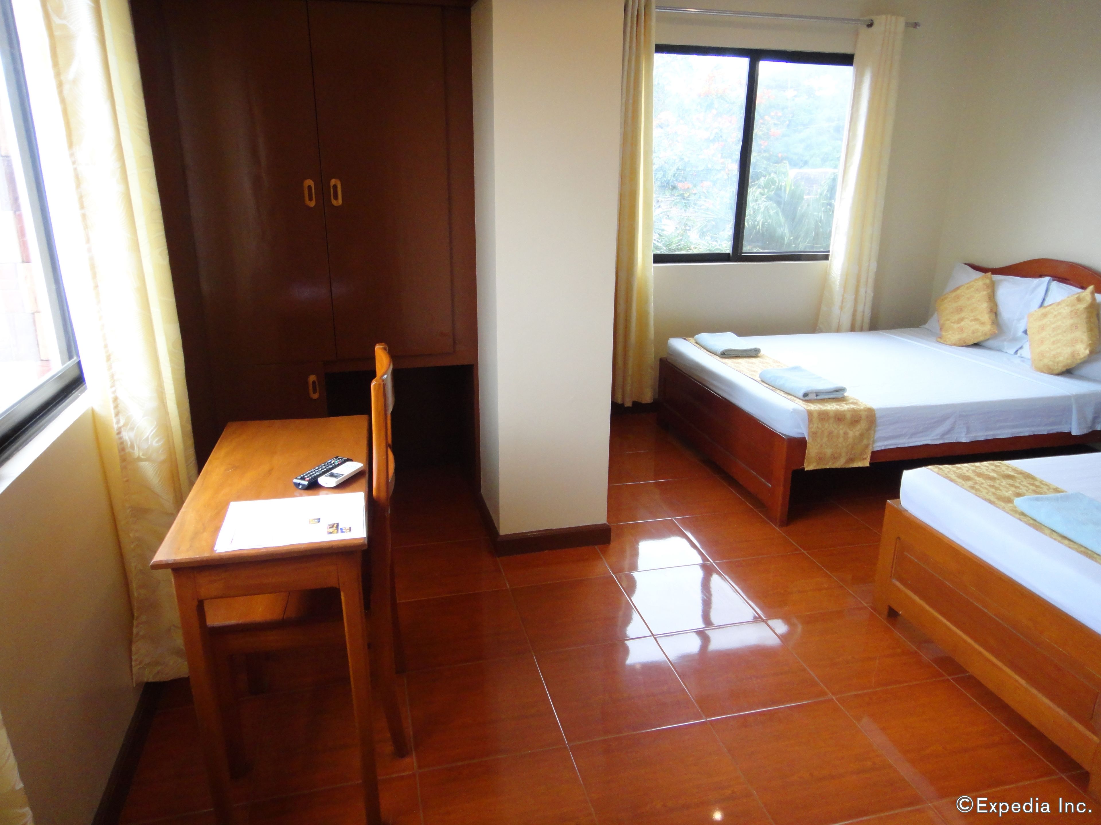 A hotel room with a wooden desk, two single beds, a wardrobe, and a window with curtains.