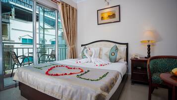 A hotel room with a bed, a nightstand, a chair, a lamp, and a balcony with chairs.