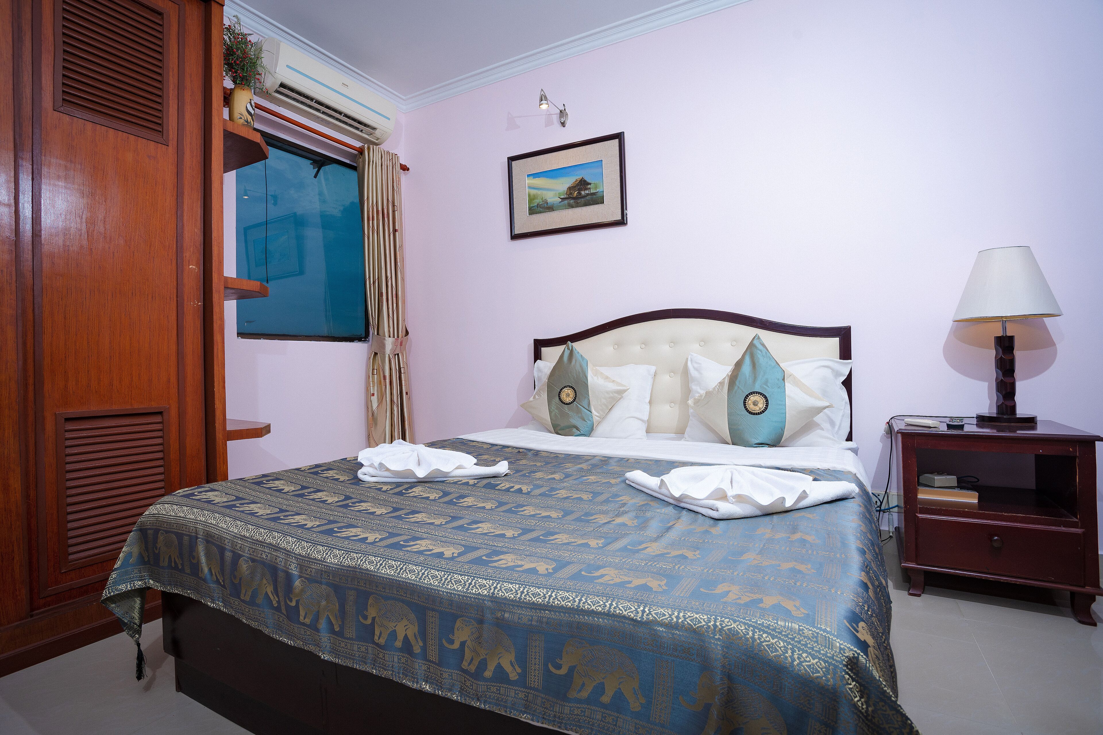 A hotel room with a bed, a nightstand, a lamp, a window with curtains, and a wall-mounted picture.
