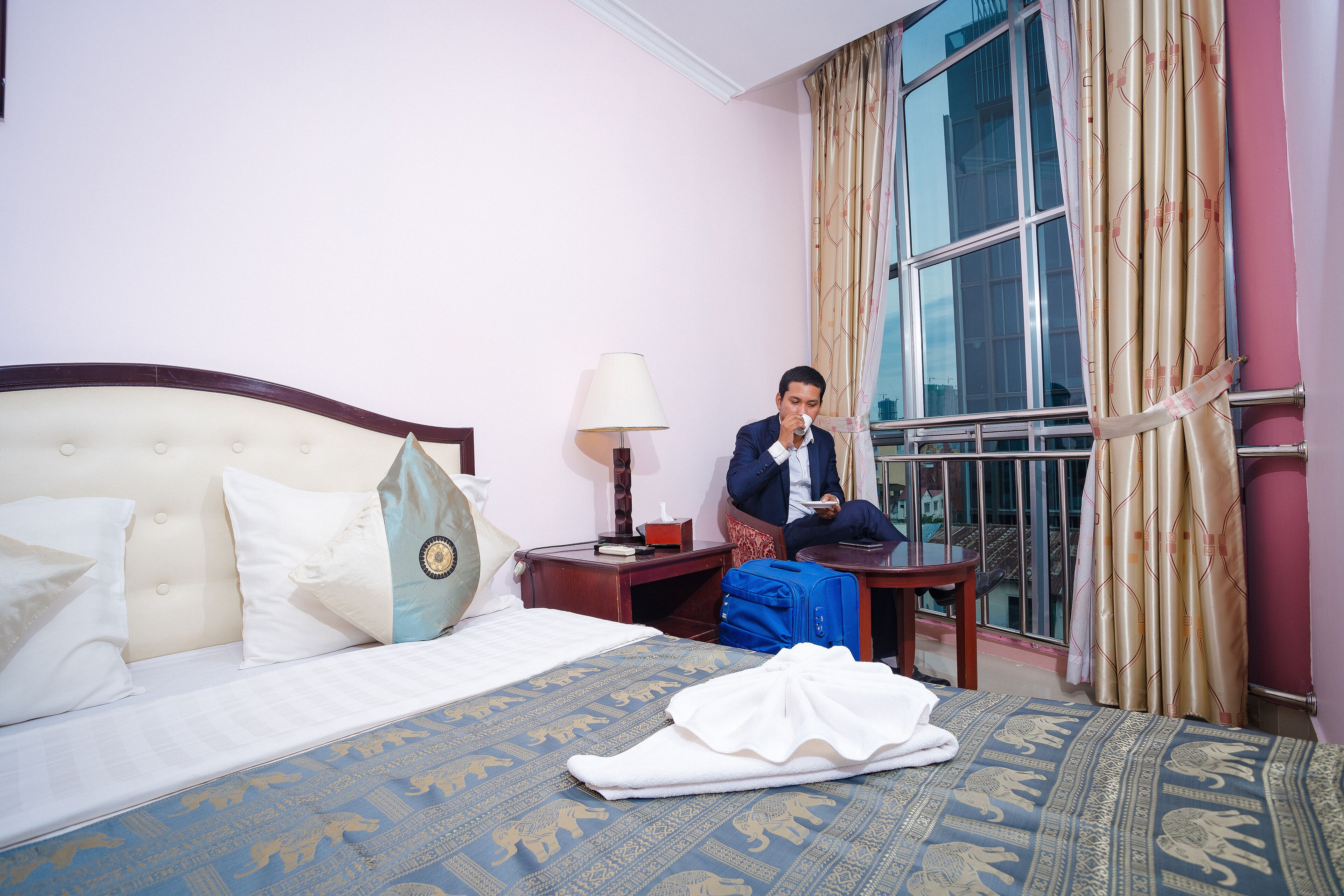 A hotel room with a bed, a nightstand, a suitcase, and a window with curtains.