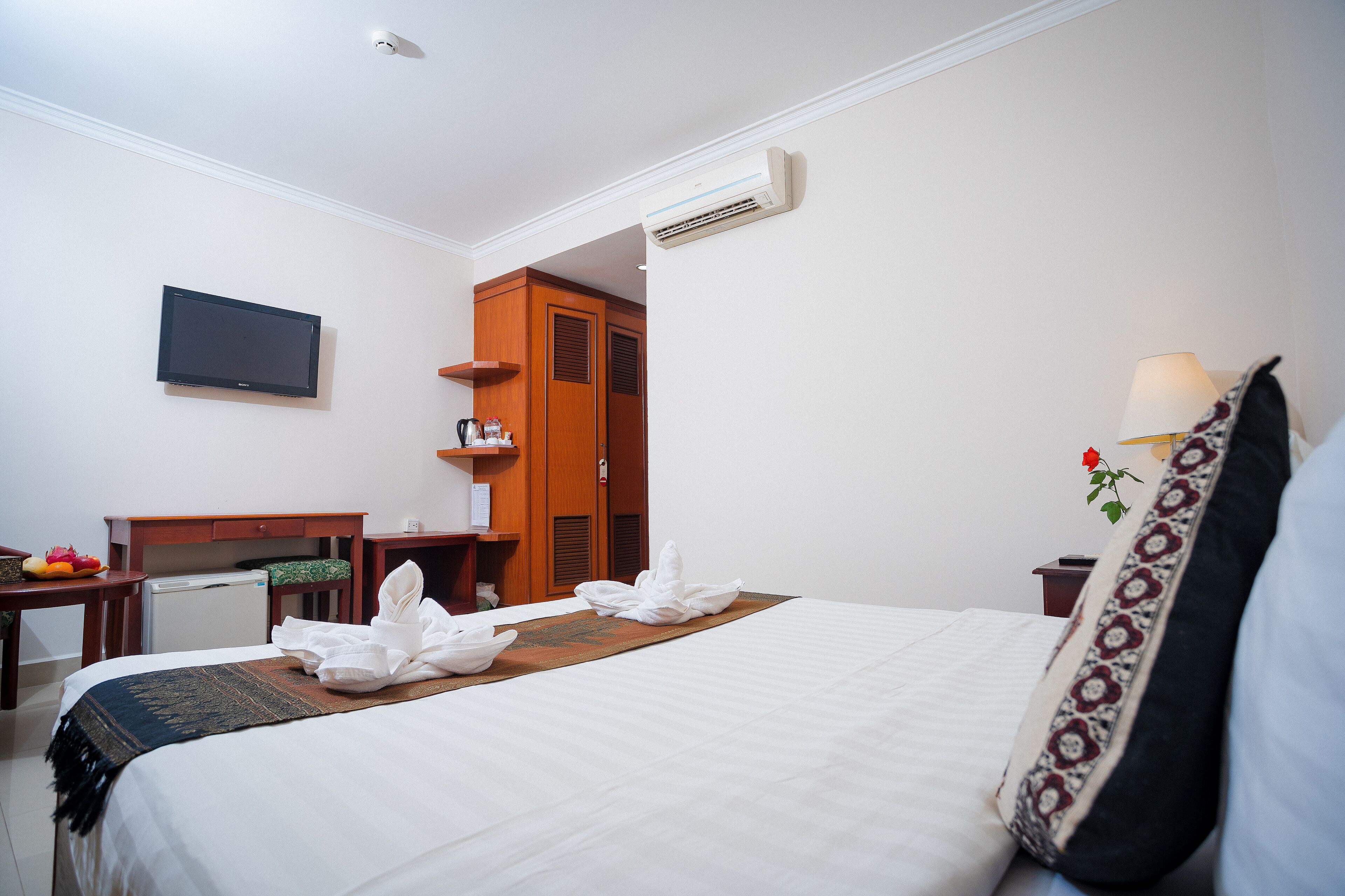 A hotel room with a bed, a desk, a television, and an air conditioning unit.