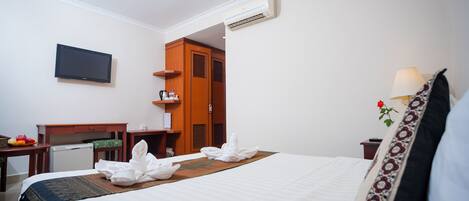 A hotel room with a bed, a desk, a television, and an air conditioning unit.