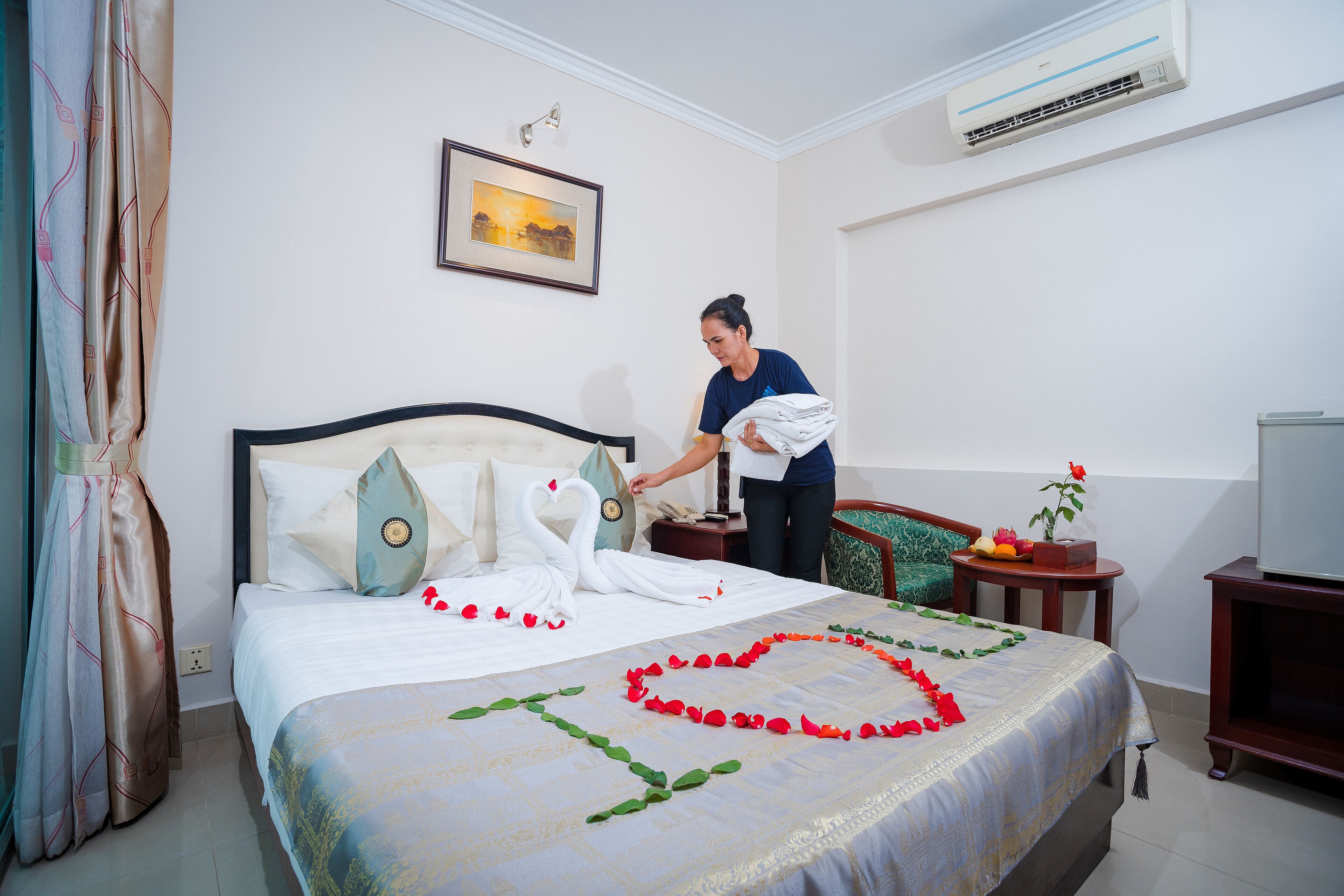 A neatly made bed with a swan and rose decorations, a framed picture on the wall, and a TV on the right.