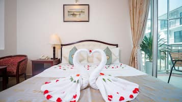 A hotel room with a bed featuring a swan-shaped towel arrangement, a framed picture on the wall, and a view of the outside balcony.