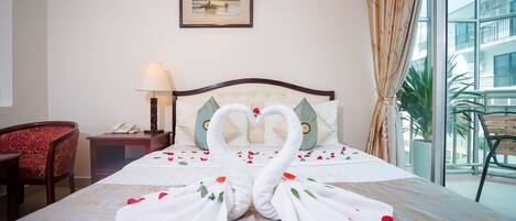 Habitación de hotel con cama, una decoración de toallas con forma de cisne, un cuadro en la pared y vistas al balcón.