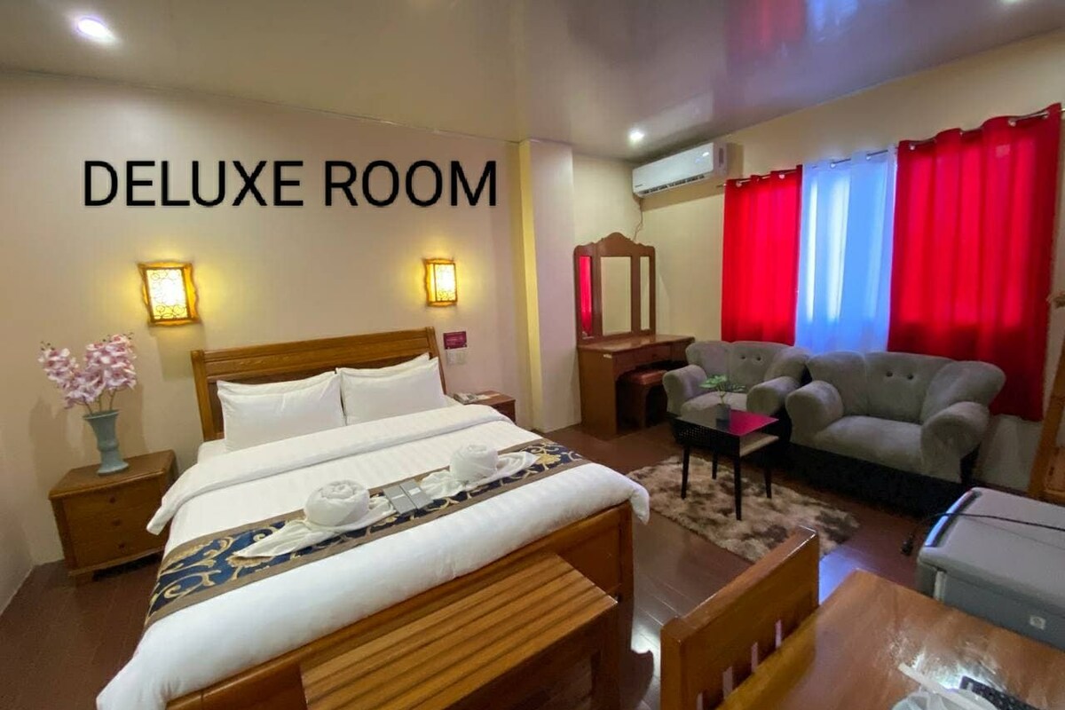Una habitación de lujo con una cama grande, mesitas de noche, un escritorio, un sofá y un televisor.