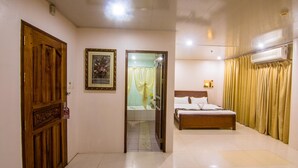 Una habitación de hotel con una puerta de madera, una cama con ropa de cama blanca, un baño con ducha y una cortina.
