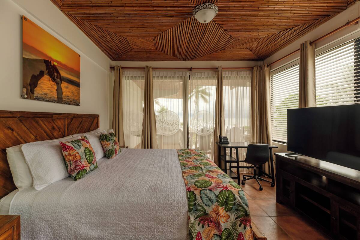 Una habitación de hotel con cama, televisión, escritorio y ventana con cortinas.