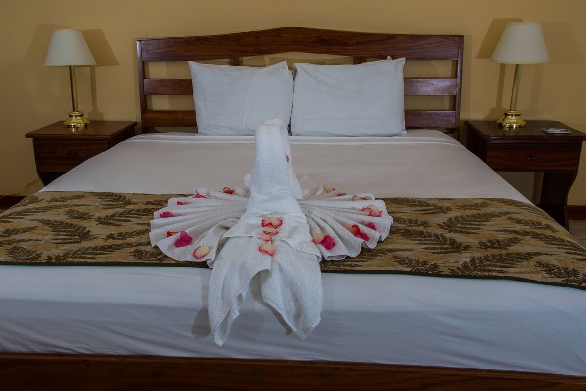 Una habitación de hotel con una cama bien hecha, dos mesitas de noche con lámparas y una colcha estampada con motivos florales.