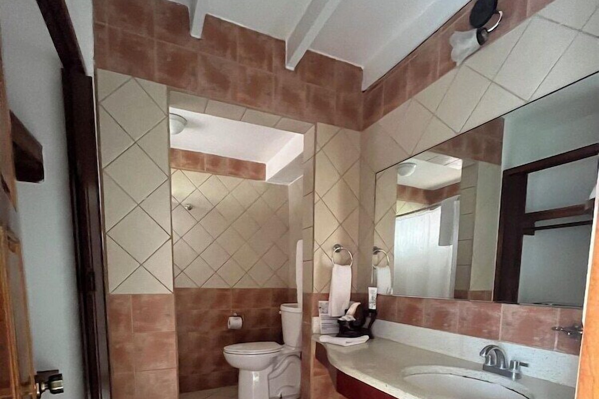 A bathroom with a toilet, sink, mirror, and tiled walls.