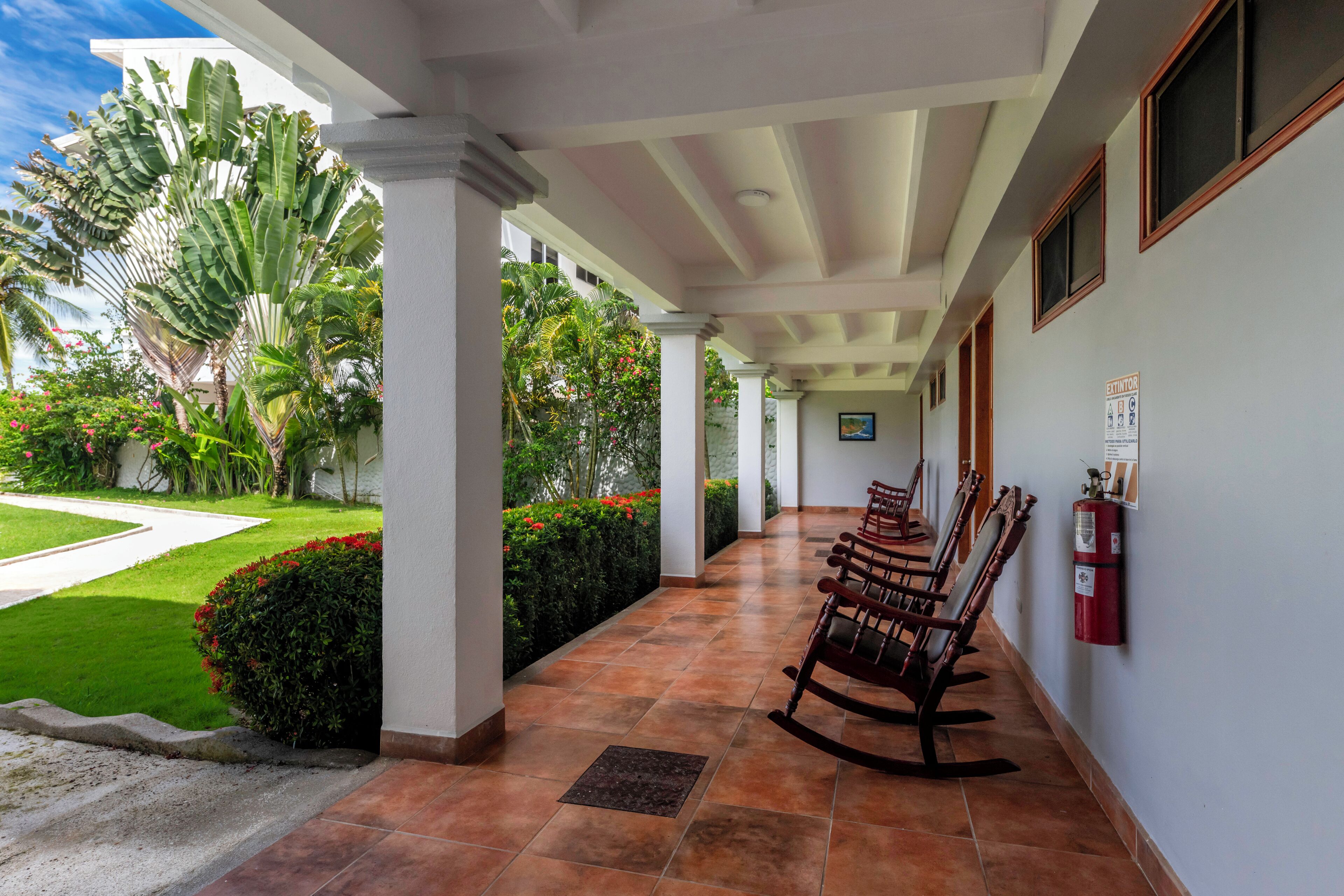 A covered outdoor area with a tiled floor, wooden rocking chairs, and a fire extinguisher on the wall.