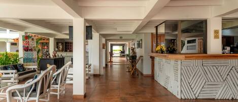 Un vestíbulo de hotel con mostrador de recepción, zona de estar y un largo pasillo que conduce a otras habitaciones.