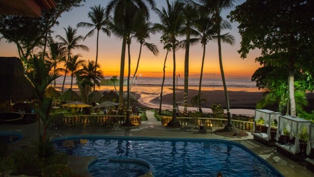 A swimming pool with a sunset view, palm trees, and beach in the background. - Jacó Laguna Resort and Beach Club (Jacó)