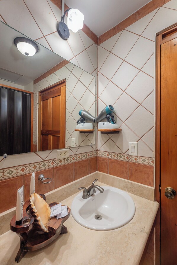Un baño con un lavamanos blanco, un espejo y un secador de pelo en un estante.