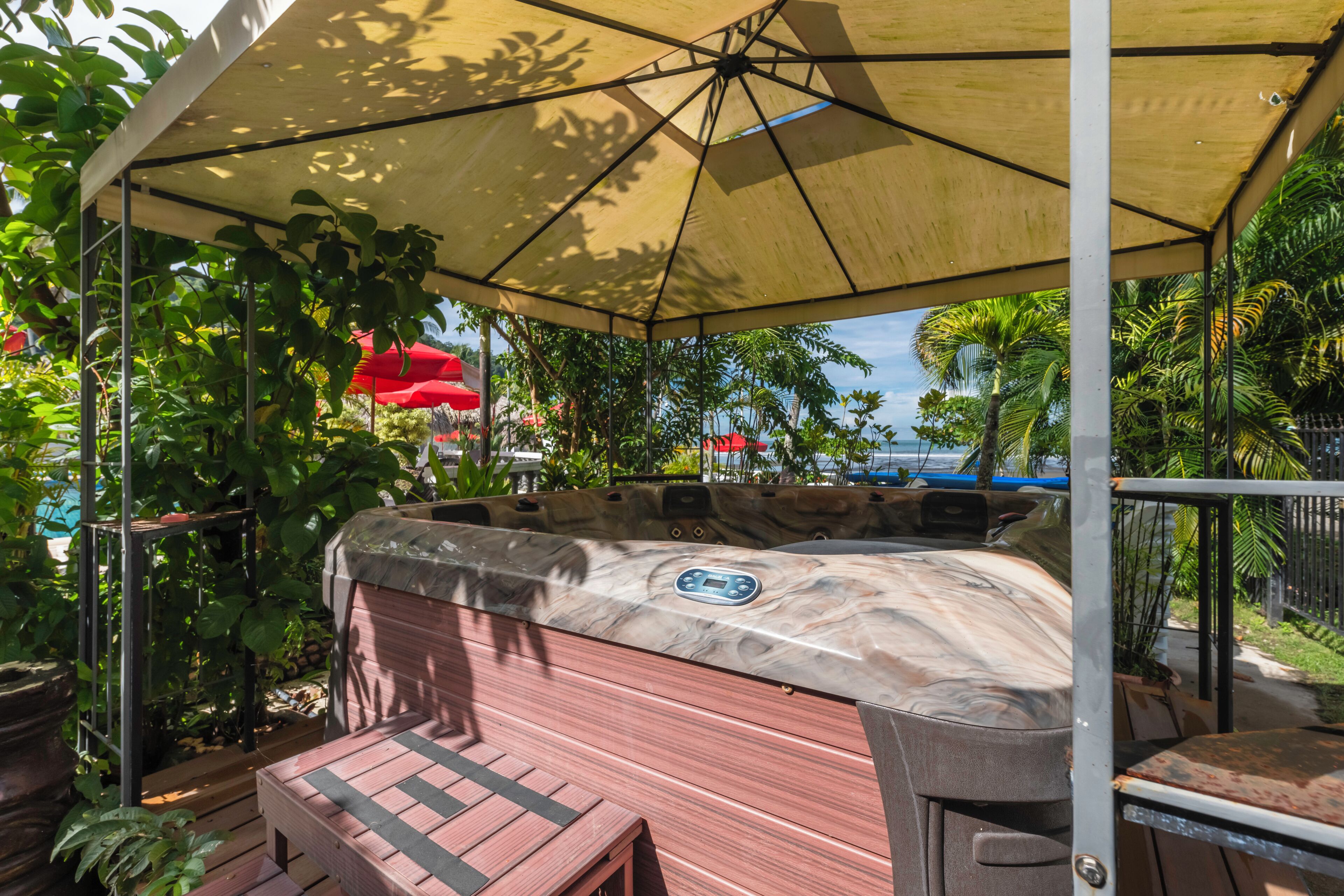 A hot tub under a canopy with a wooden deck and potted plants.