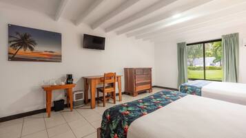 Habitación de hotel con dos camas, un escritorio con silla, cafetera, televisión en la pared y un cuadro de un atardecer.