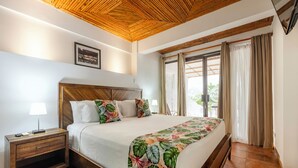 A bedroom with a wooden headboard, a bed with a floral bedspread, a nightstand with a lamp, and a window with curtains. - Jacó Laguna Resort and Beach Club (Jacó)