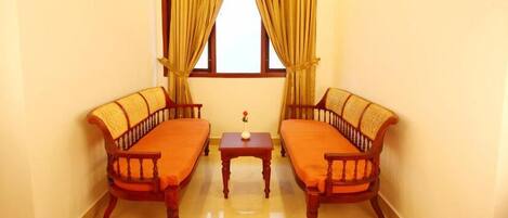 A room with two wooden sofas, a small table, and a window with curtains.