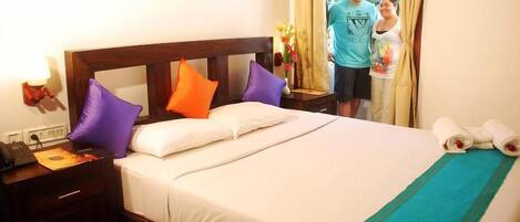 A hotel room with a bed, a nightstand with a lamp, a telephone, and a window with curtains.