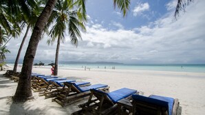 A beach with wooden lounge chairs and palm trees. - Sea Wind Resort (Boracay Island)