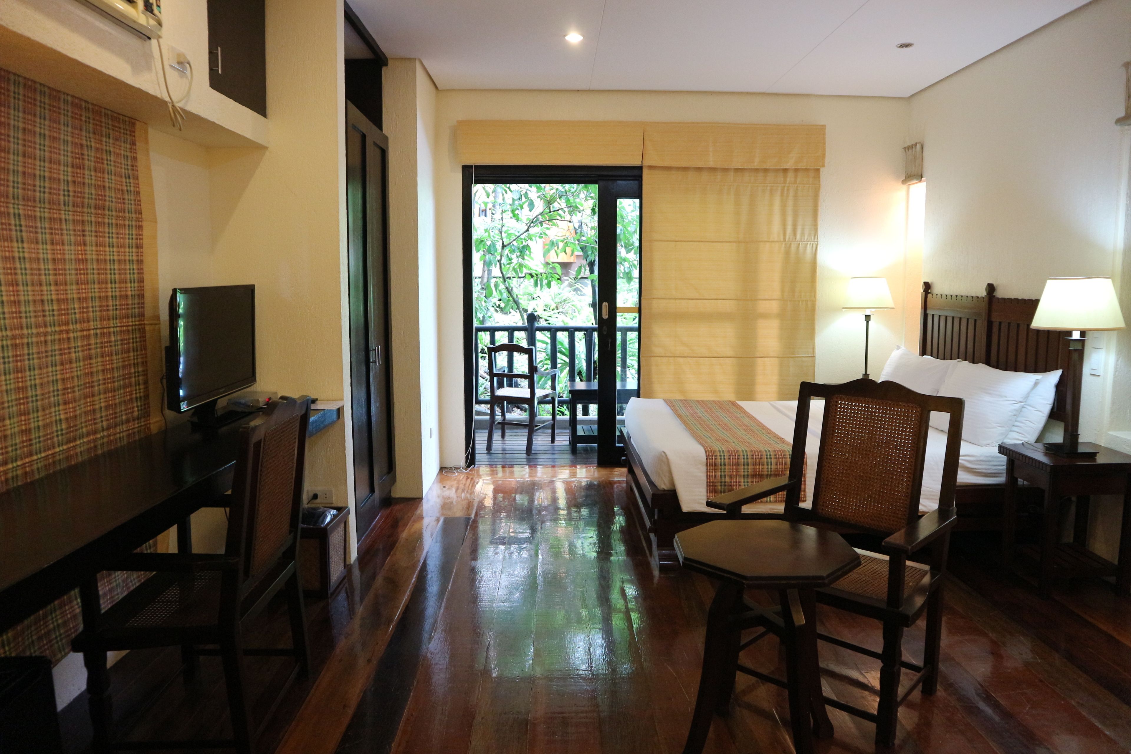 Habitación de hotel con cama, escritorio, silla, televisión y balcón con vistas a zonas verdes.