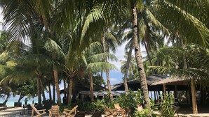 A beach with palm trees, wooden chairs, and a covered area with a thatched roof. - Sea Wind Resort (Boracay Island)