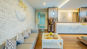 A modern hotel lobby with a white brick wall, a reception desk, a seating area with a sofa and coffee table, and a wooden floor. - The Rubber Hotel Phuket (Thep Krasattri)