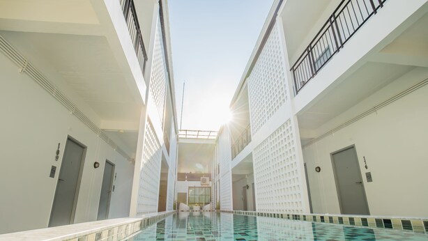 A swimming pool with a tiled floor and a glass railing, surrounded by white walls and doors. - The Rubber Hotel Phuket (Thep Krasattri)