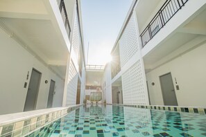 A swimming pool with a tiled floor and a glass railing, surrounded by white walls and doors. - The Rubber Hotel Phuket (Thep Krasattri)