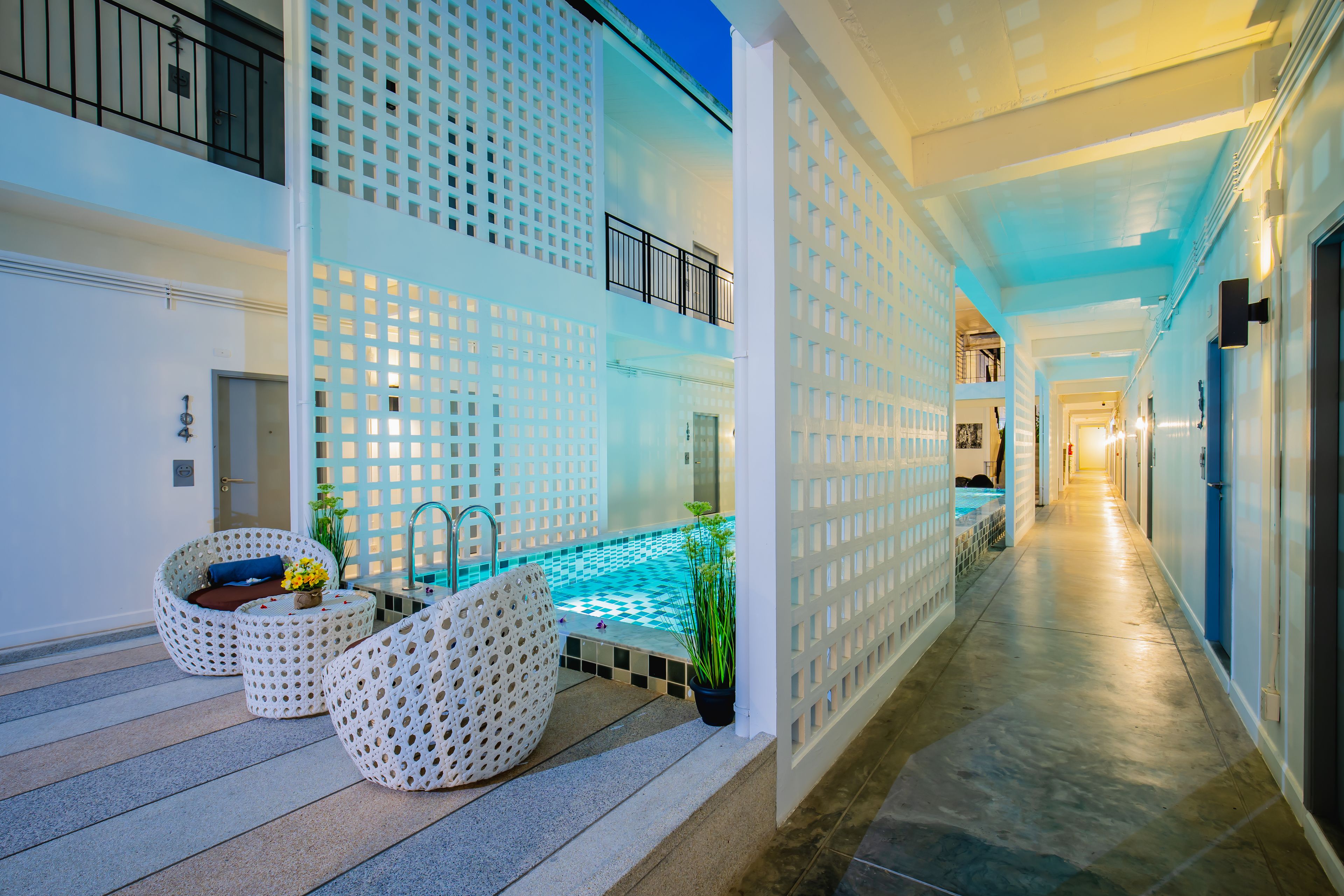 Un pasillo moderno de hotel con zona de piscina, mobiliario blanco estampado e iluminación azul.