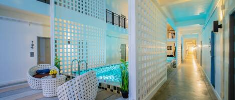 A modern hotel corridor with a pool area, white patterned furniture, and a blue-lit interior.
