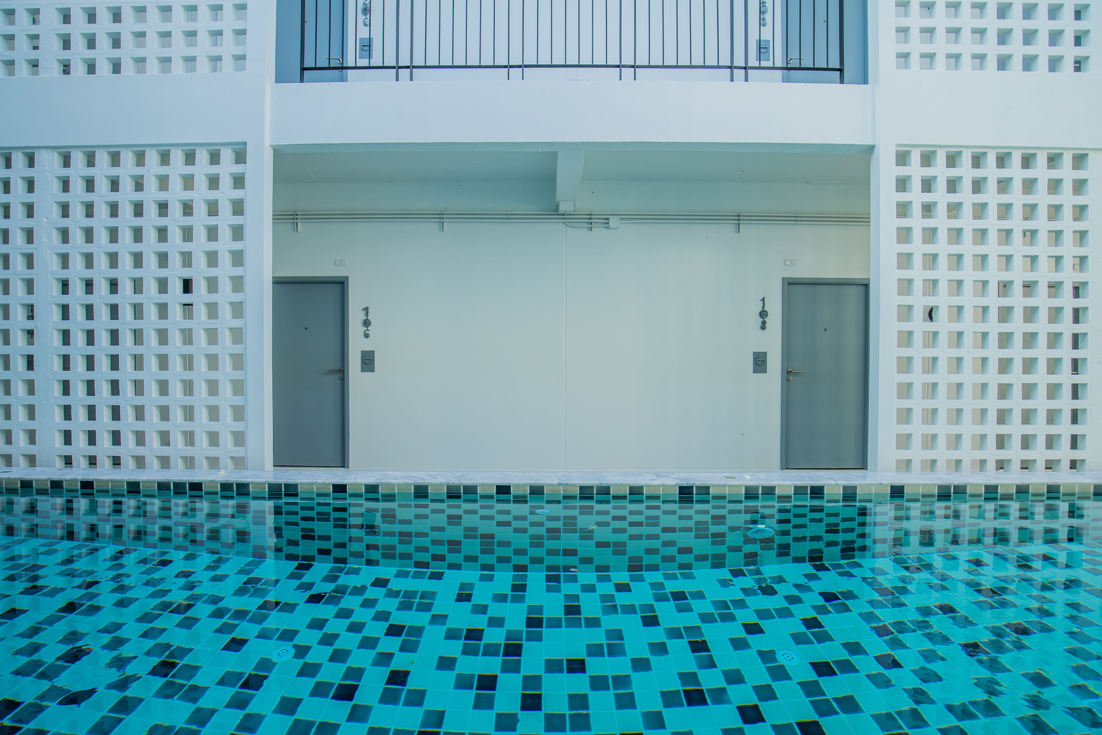 Una piscina interior moderna con un diseño geométrico de azulejos, dos puertas y una pared blanca con un patrón de rejilla.