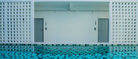 Una piscina interior moderna con un diseño geométrico de azulejos, dos puertas y una pared blanca con un patrón de rejilla.