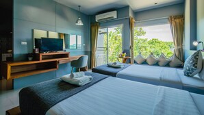 A hotel room with two beds, a desk with a TV, and a balcony with a view of greenery. - The Rubber Hotel Phuket (Thep Krasattri)