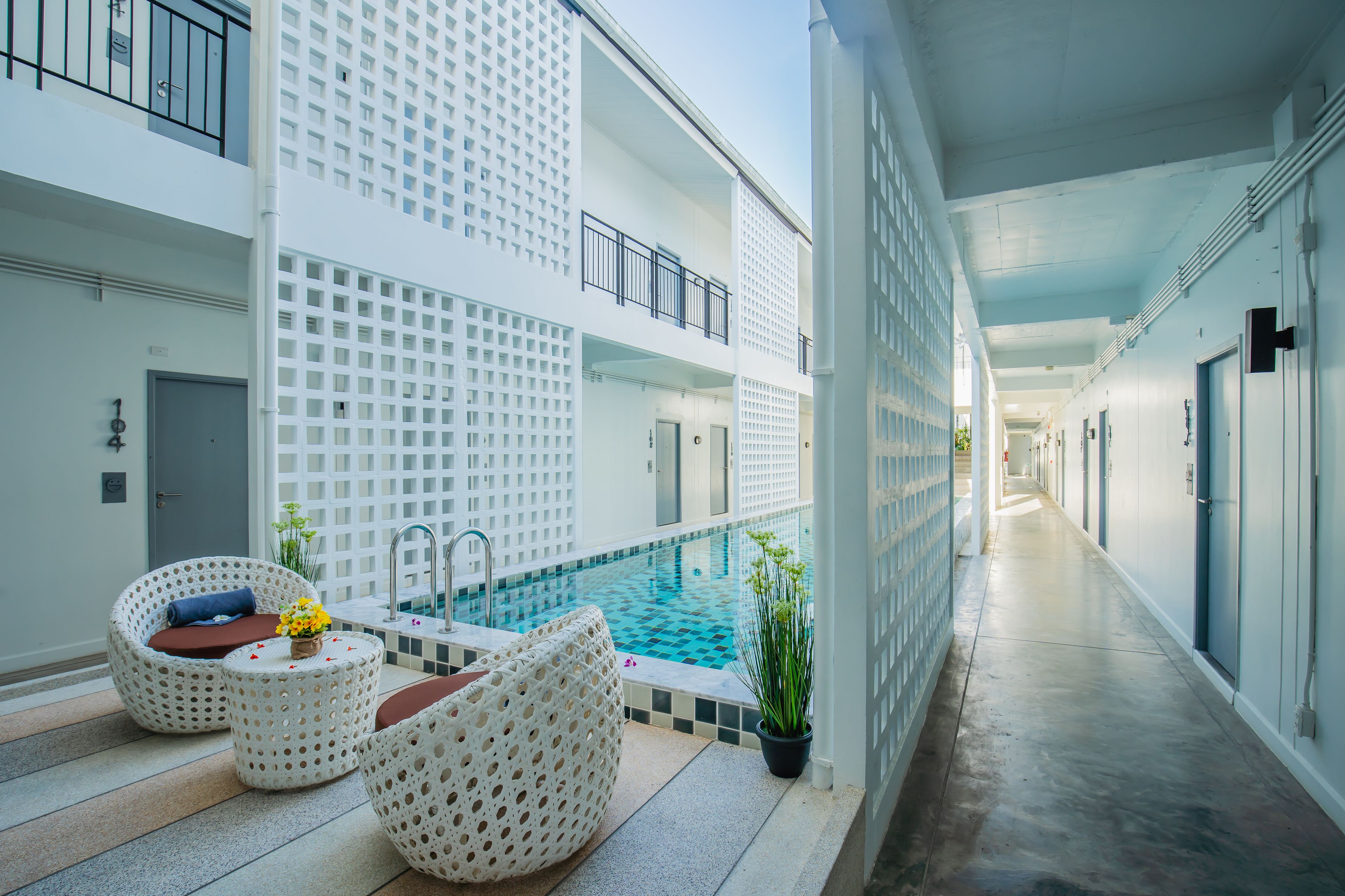 Un hotel moderno con area piscina, inclusi lettini e un tavolino con fiori.