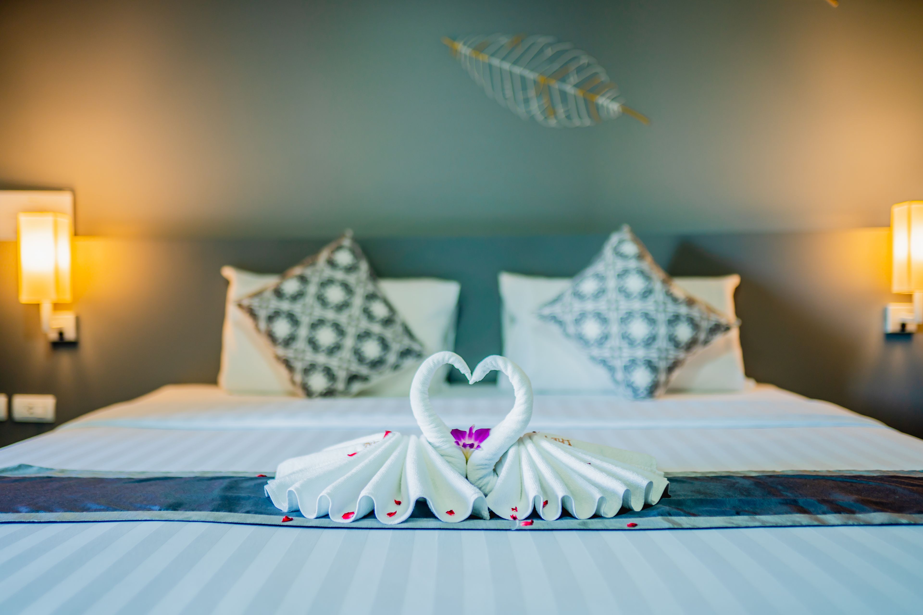 A neatly made bed with a heart-shaped towel arrangement and decorative pillows.