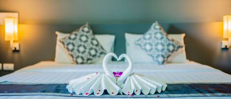 A neatly made bed with a heart-shaped towel arrangement and decorative pillows.