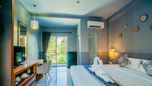 A modern hotel room with a large bed, a desk with a computer, a TV, and a balcony with a view of greenery. - The Rubber Hotel Phuket (Thep Krasattri)