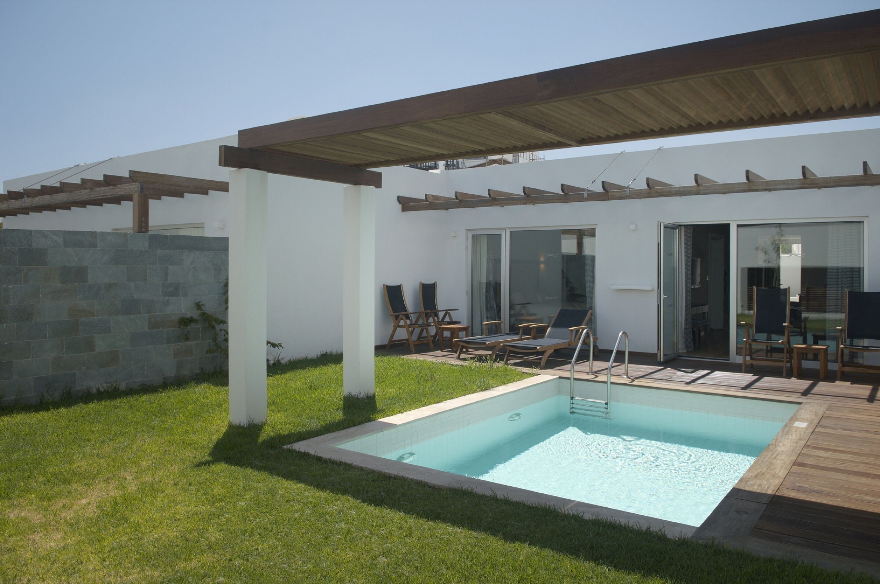 A modern outdoor pool area with a wooden deck, lounge chairs, and a covered patio.
