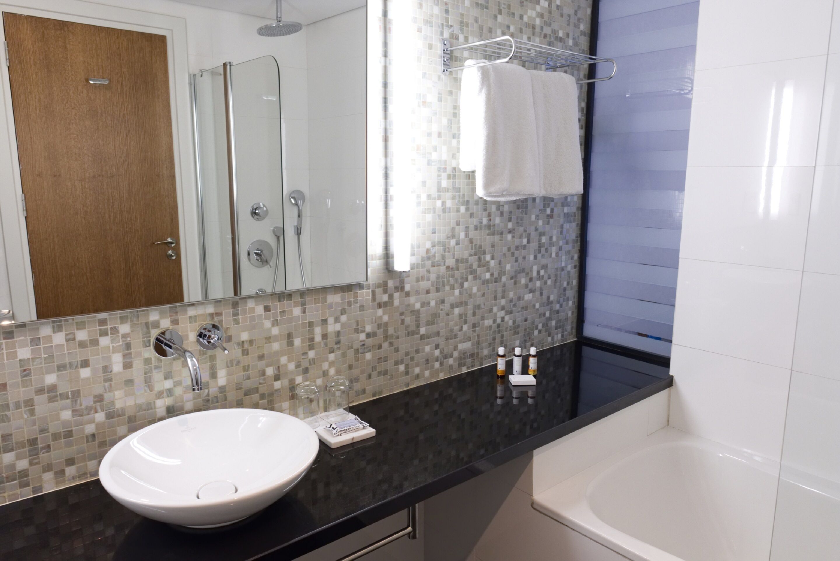 Un baño moderno con un espejo grande, un lavabo blanco, una ducha y una bañera.