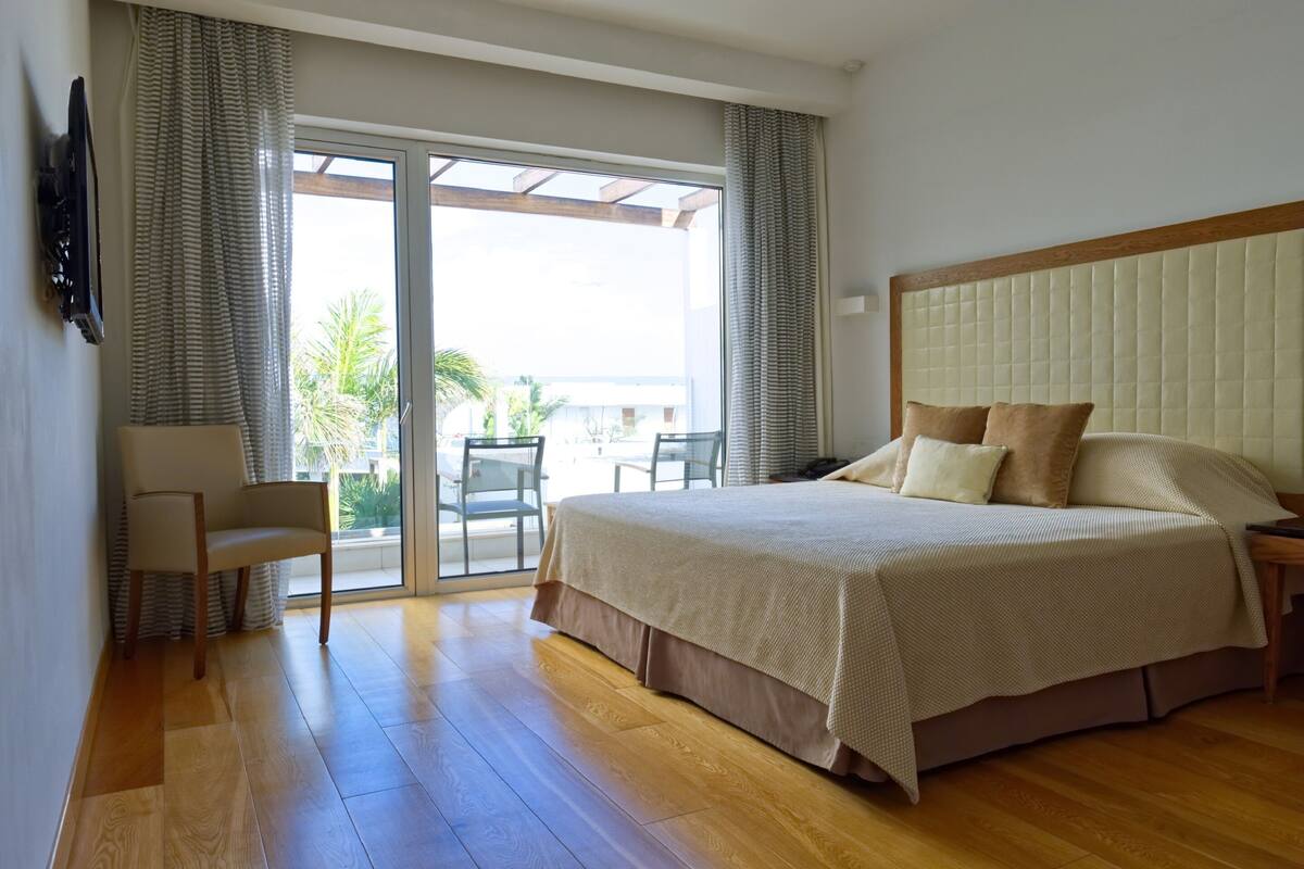 Une chambre d’hôtel avec un grand lit, une chaise, un téléviseur fixé au mur et une porte-fenêtre coulissante donnant sur un espace extérieur.