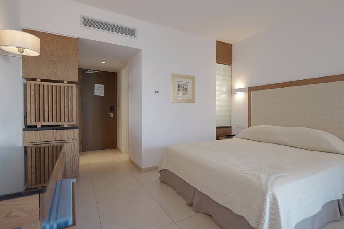 Une chambre d’hôtel avec un grand lit, une table de chevet avec un téléphone, une armoire en bois et un tableau au mur.